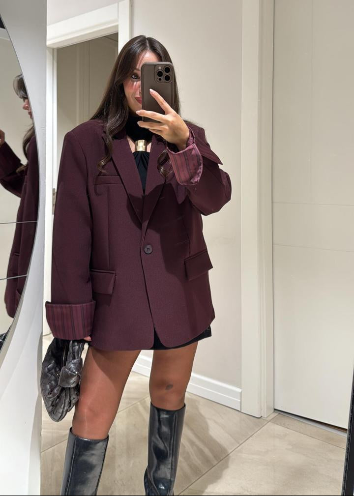 Ce blazer oversize pour femme, d’une élégante teinte aubergine, est une pièce moderne et polyvalente, parfaite pour un look décontracté chic ou plus habillé. Sa coupe ample et légèrement structurée offre un confort optimal et une silhouette contemporaine.
Il présente un col à revers classique et une fermeture à un seul bouton foncé.

La particularité de ce blazer réside dans sa doublure rayée (blanc et marron/rose pâle), qui devient visible lorsque les manches sont retroussées ou lorsque le blazer est légèr
